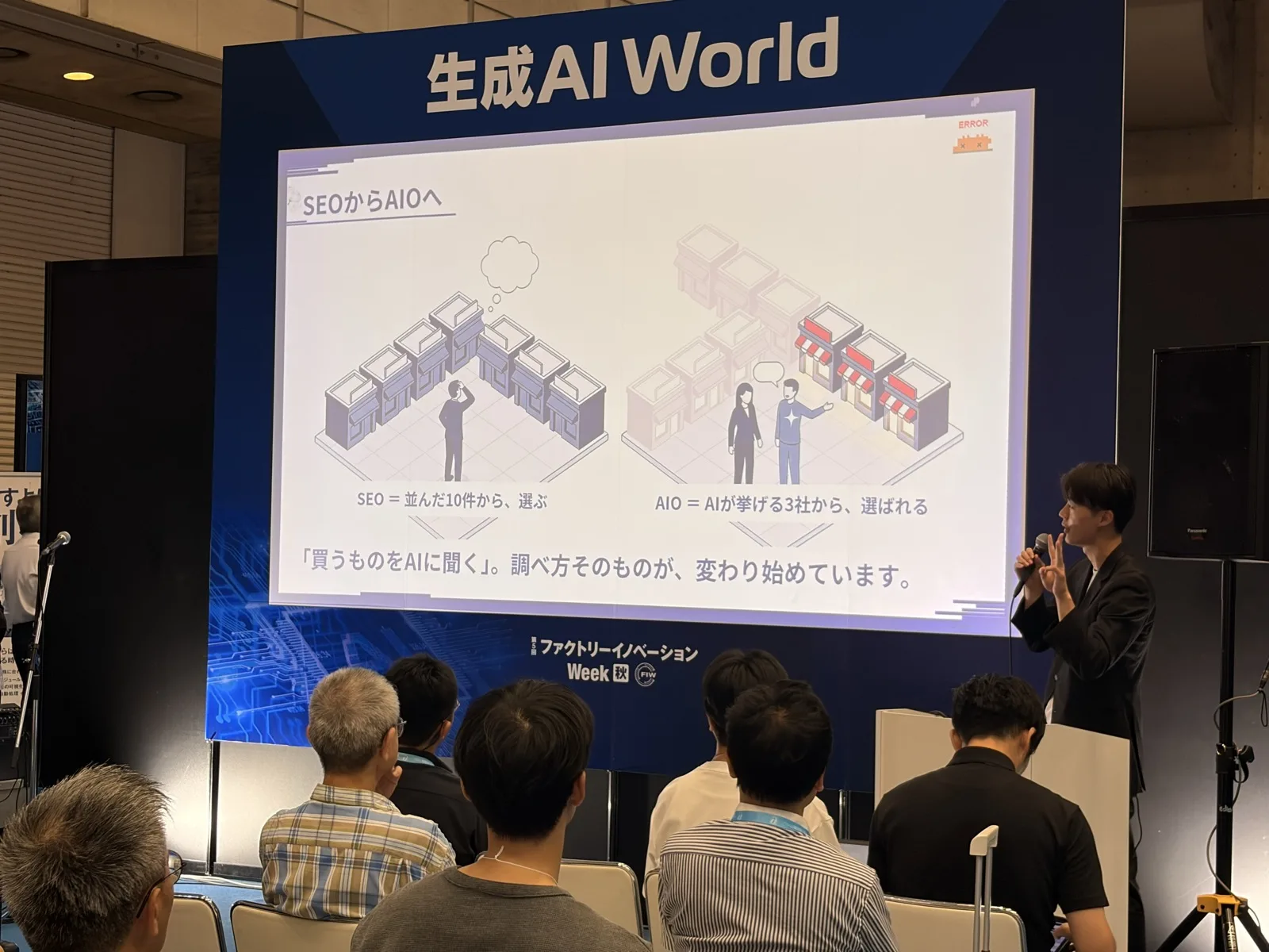 生成AI Worldのセミナー会場で、代表の松浦が「SEOからAIOへ」のスライドを使って講演している様子